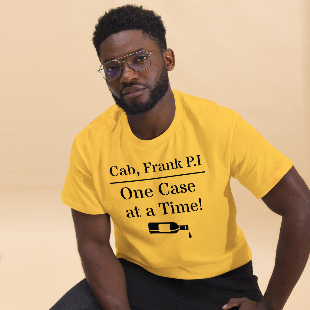 Yellow cotton t-shirt with bold black text reading “Cab, Frank. P.I. – One Case at a Time,” styled with vintage wine bottles, corks, and noir props like sunglasses and a magnifying glass to evoke detective satire and vineyard mystery.