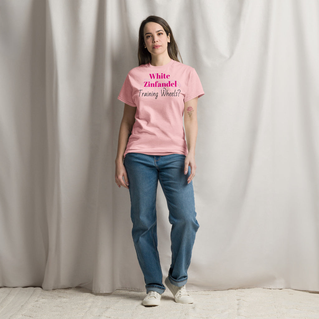 Pink White Zinfandel – Training Wheels tee laid flat on a rustic wood surface, featuring bold satirical text in vintage script. A soft blush-pink cotton shirt that hints at wine-fueled nostalgia and emotional rites of passage.