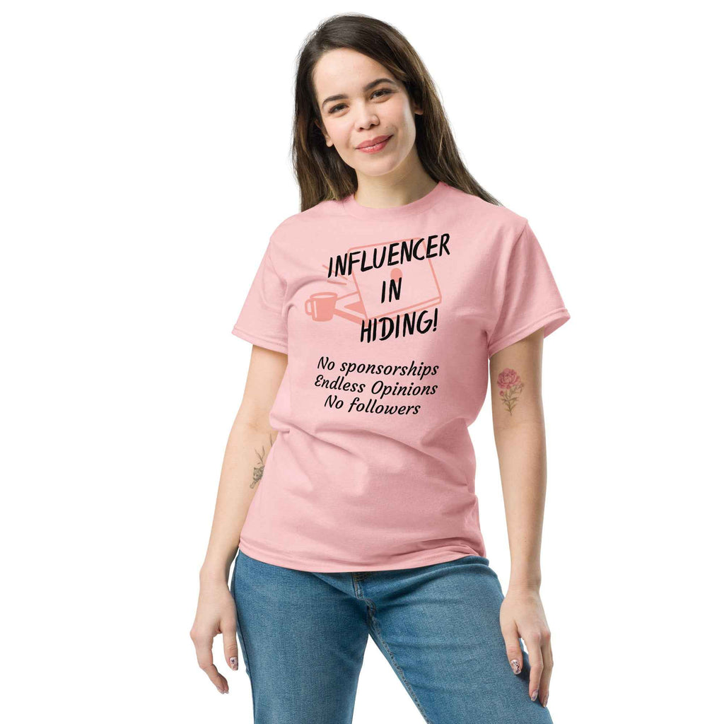 Pink T-shirt featuring a dark red, hand-drawn graphic of a laptop and coffee mug with bold text reading “INFLUENCER IN HIDING.” The design evokes remote work and digital satire—no sponsorships, no followers, just unapologetic opinions.