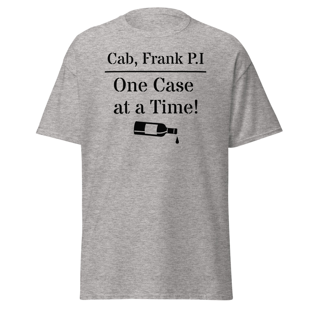 Gray cotton t-shirt with bold black text reading “Cab, Frank. P.I. – One Case at a Time,” styled with vintage wine bottles, corks, and noir props like sunglasses and a magnifying glass to evoke detective satire and vineyard mystery.