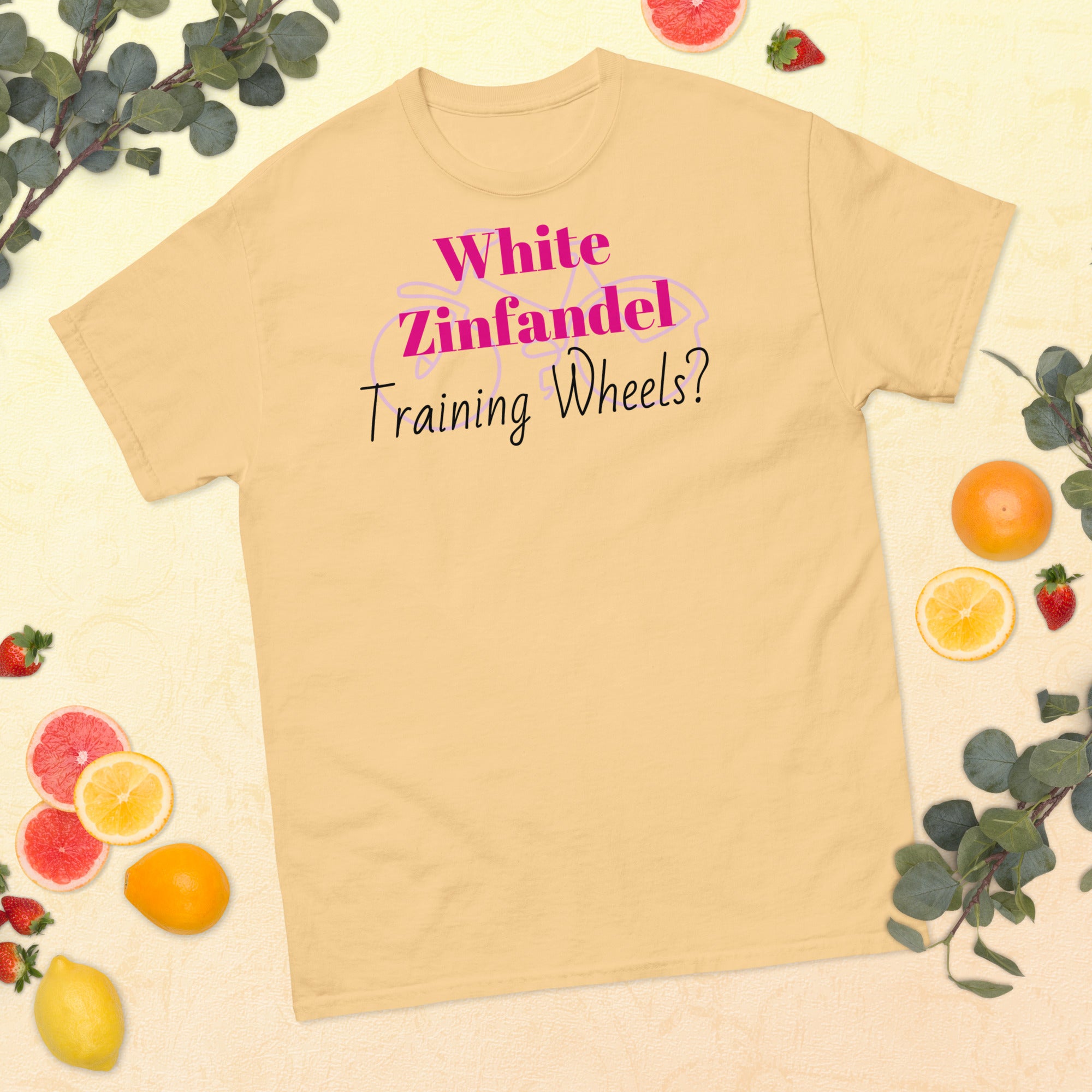 Yellow White Zinfandel – Training Wheels tee laid flat on a rustic wood surface, featuring bold satirical text in vintage script. A soft blush-pink cotton shirt that hints at wine-fueled nostalgia and emotional rites of passage.