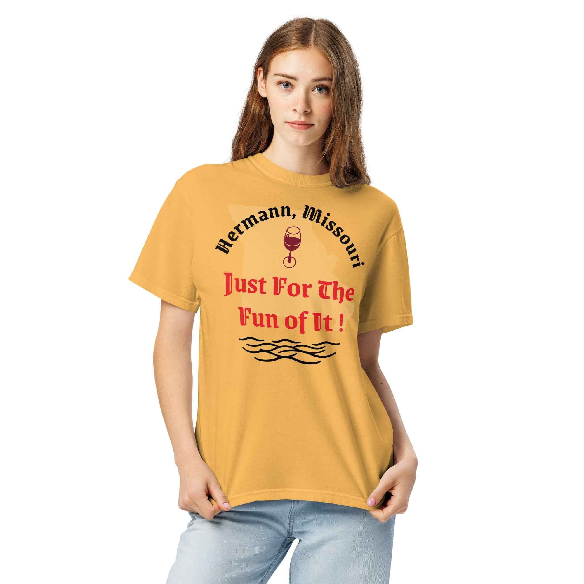 Yellow cotton t-shirt with bold black text reading “Hermann, Missouri – Just for the Fun of It!” styled with wine glasses, river maps, and vintage postcards to evoke spontaneous travel and regional charm.