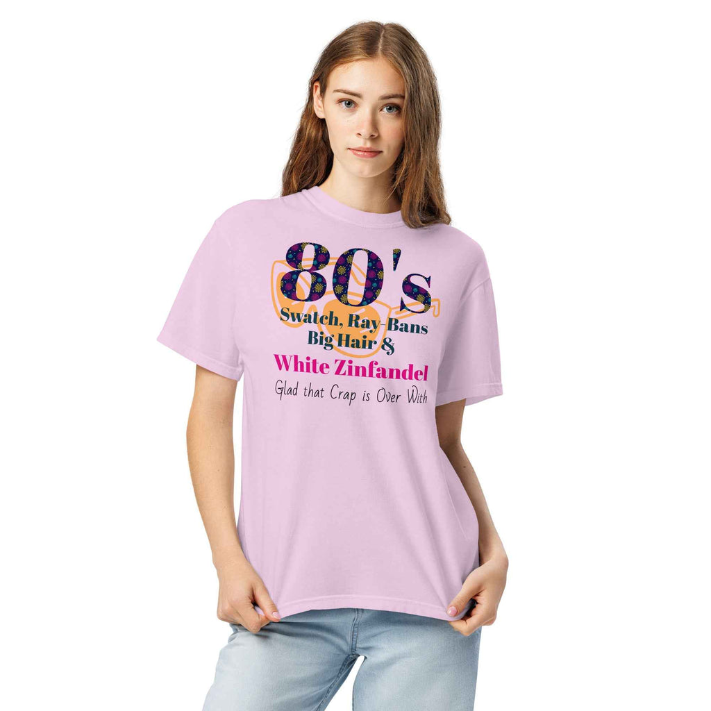 Pink T-shirt with colorful text listing 1980s trends—Swatch, Ray-Bans, big hair, and White Zinfandel—followed by the punchline “Glad that crap is over with.” A humorous nod to retro excess.