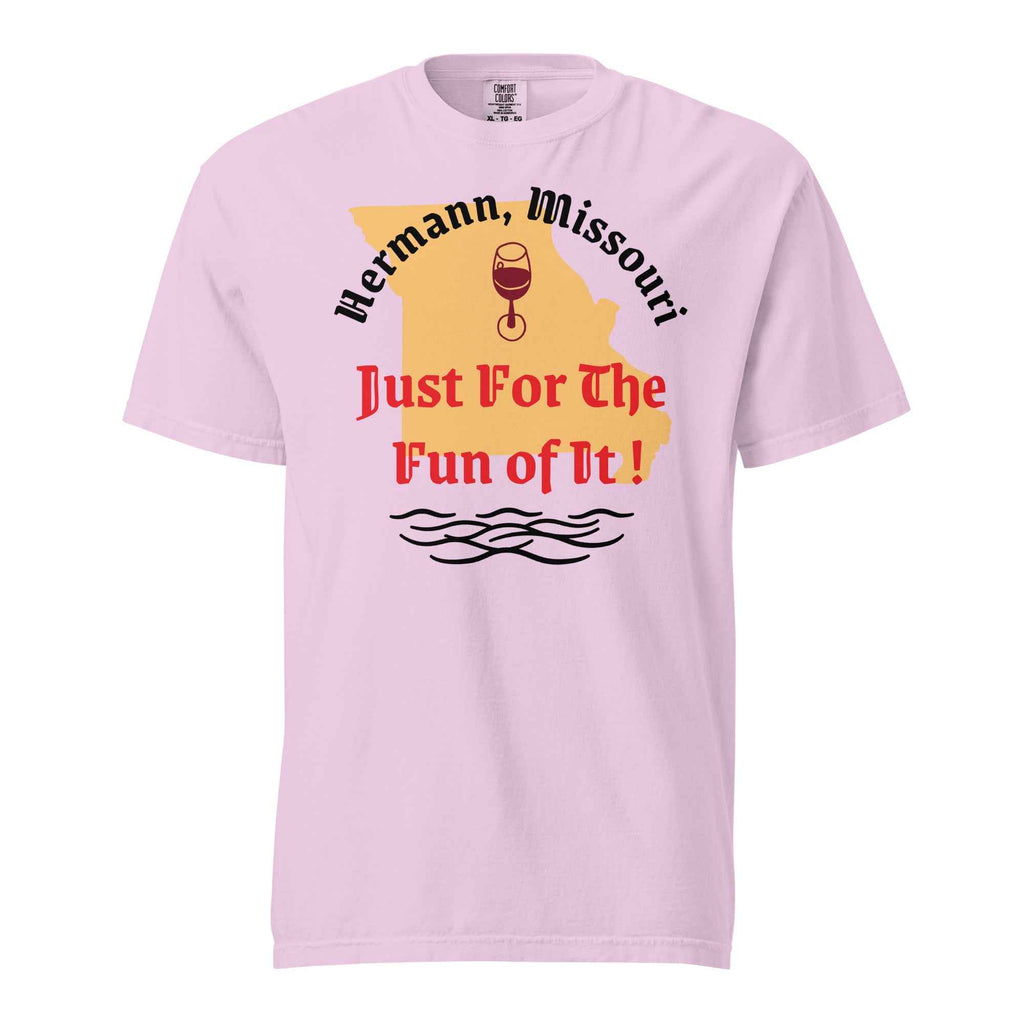 Pink cotton t-shirt with bold black text reading “Hermann, Missouri – Just for the Fun of It!” styled with wine glasses, river maps, and vintage postcards to evoke spontaneous travel and regional charm.